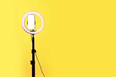 Photo of Ring lamp with smartphone on orange background, space for text