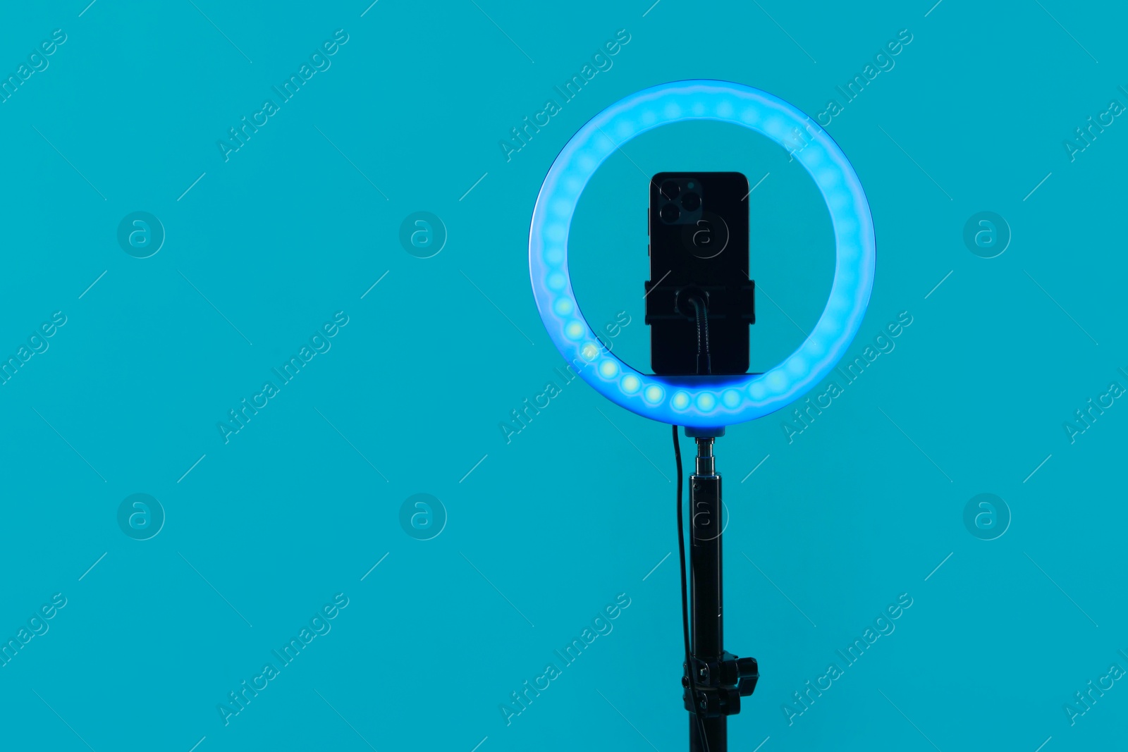 Photo of Ring lamp with smartphone on light blue background, space for text