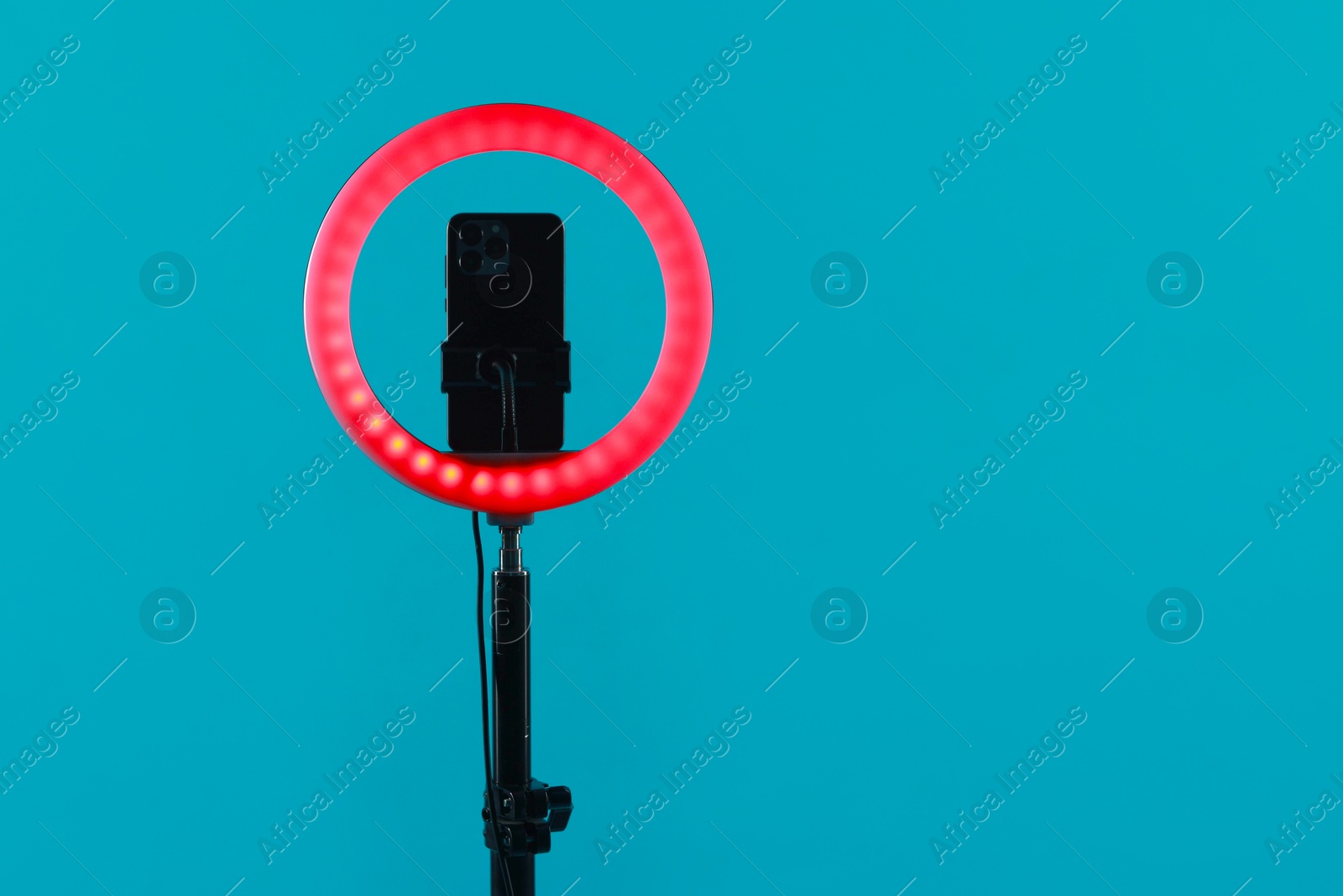 Photo of Ring lamp with smartphone on light blue background, space for text