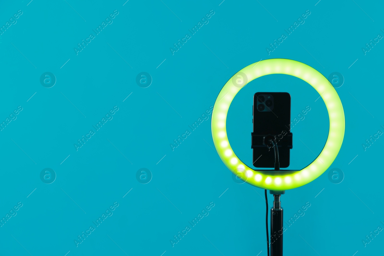 Photo of Ring lamp with smartphone on light blue background, space for text