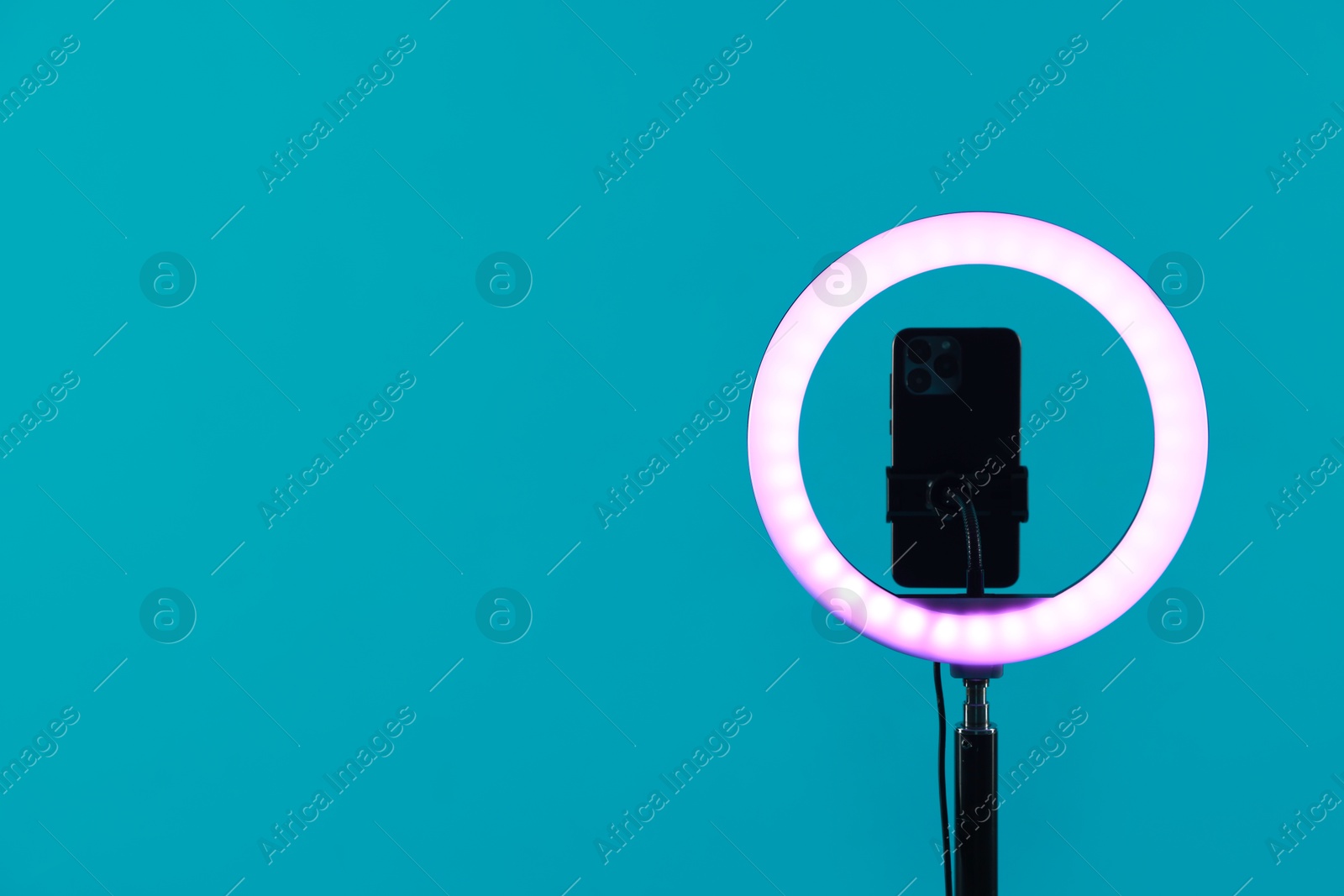 Photo of Ring lamp with smartphone on light blue background, space for text