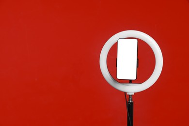 Photo of Ring lamp with smartphone on red background, space for text