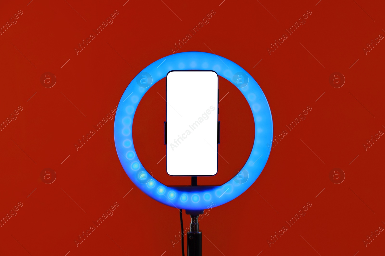 Photo of Ring lamp with smartphone on red background