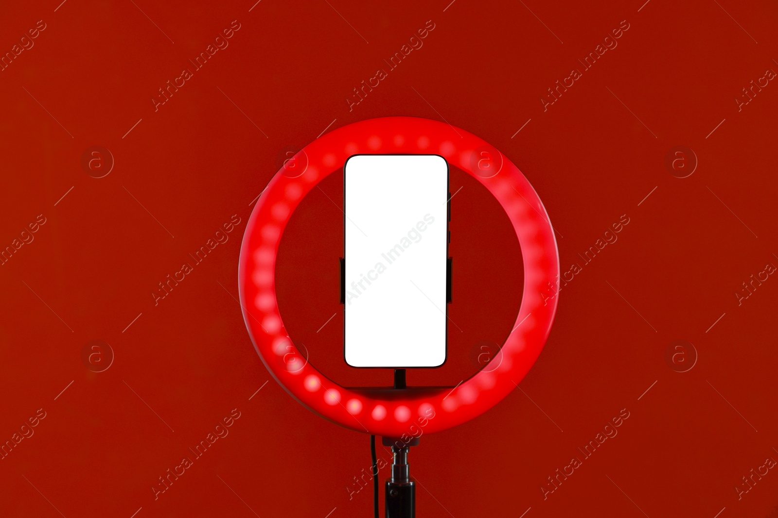 Photo of Ring lamp with smartphone on red background