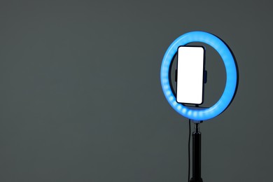 Photo of Ring lamp with smartphone on grey background, space for text