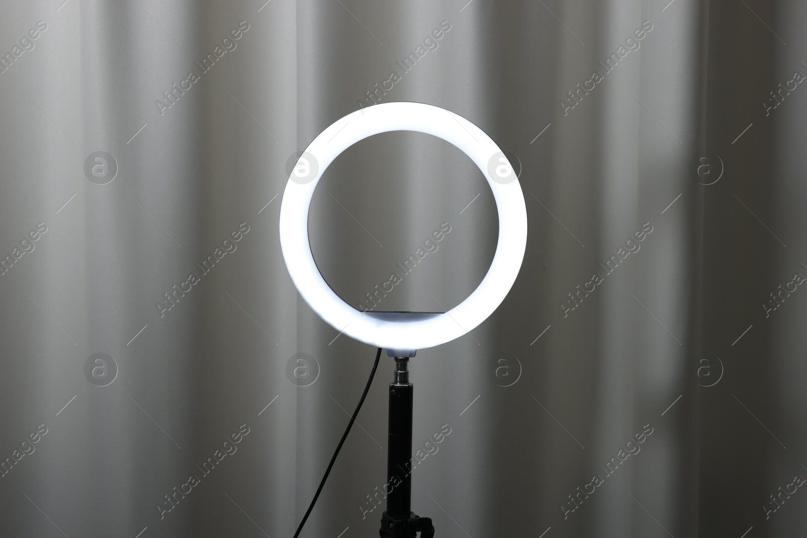 Photo of One glowing ring lamp near grey curtain