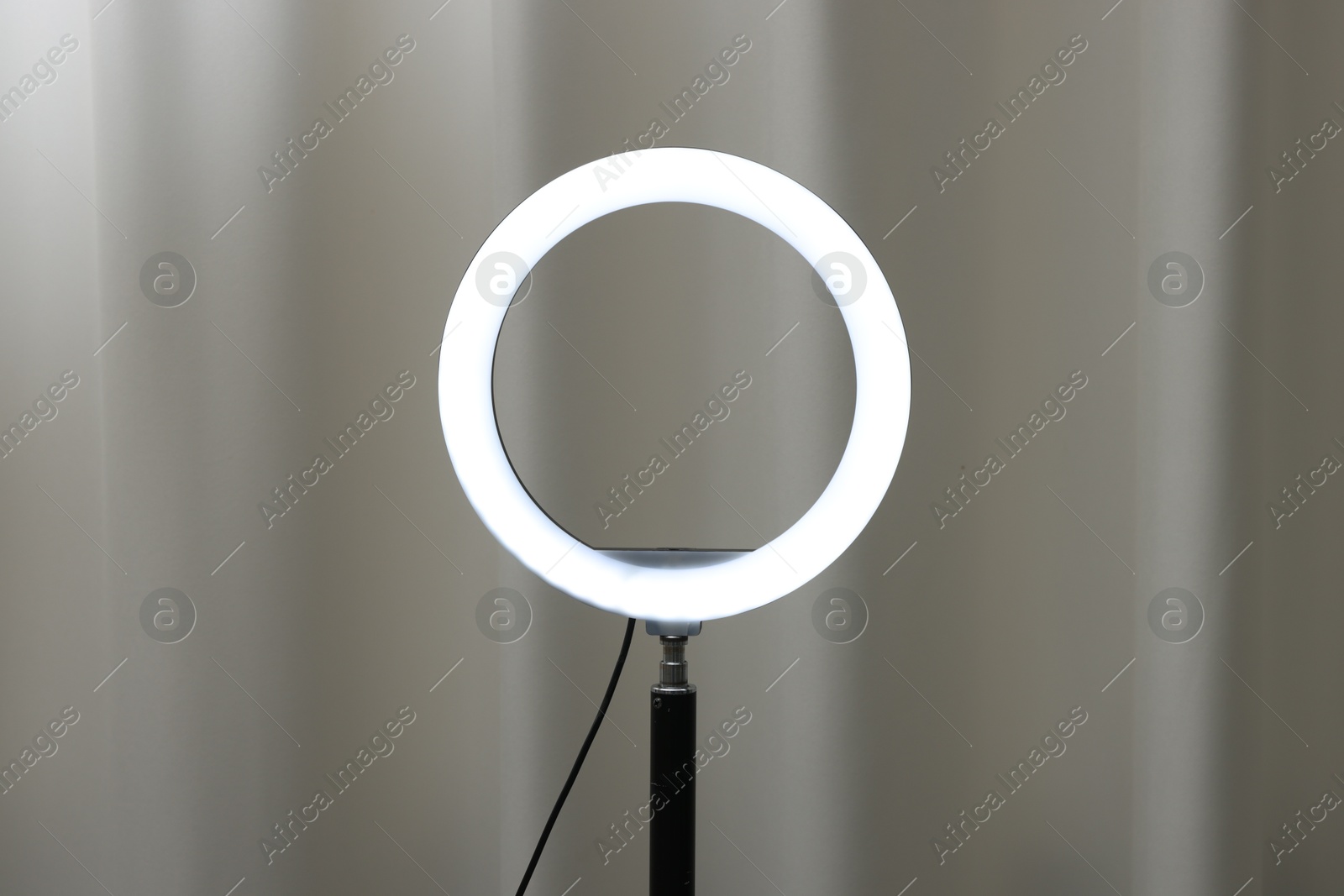 Photo of One glowing ring lamp near grey curtain