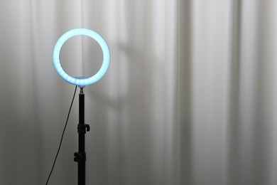 Photo of One glowing ring lamp near grey curtain. Space for text