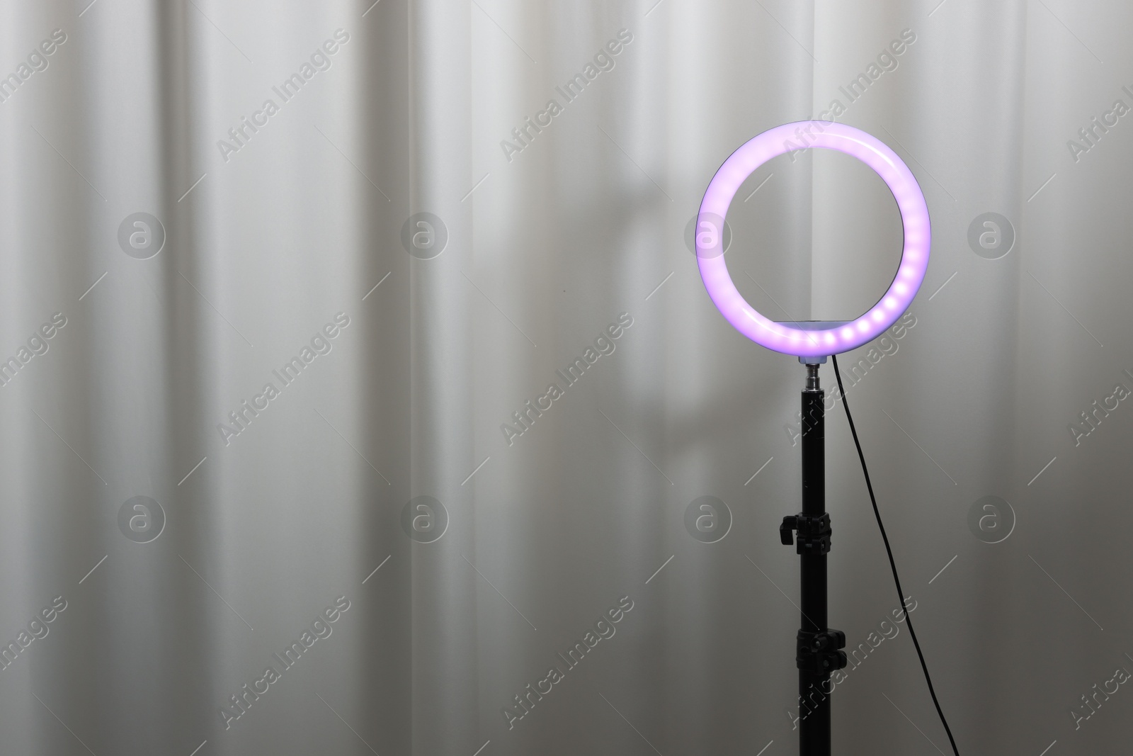 Photo of One glowing ring lamp near grey curtain. Space for text