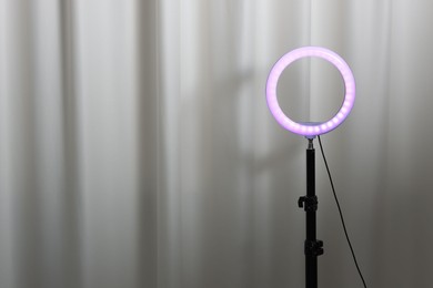 Photo of One glowing ring lamp near grey curtain. Space for text