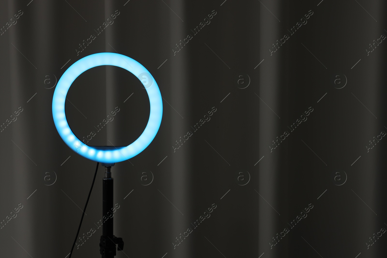 Photo of One glowing ring lamp near black curtain. Space for text