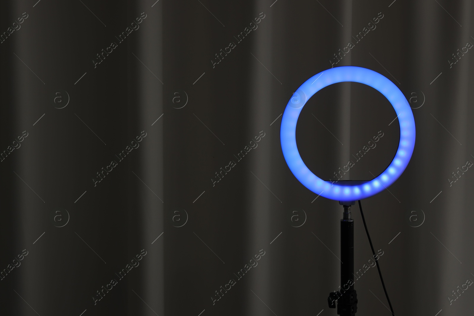 Photo of One glowing ring lamp near black curtain. Space for text