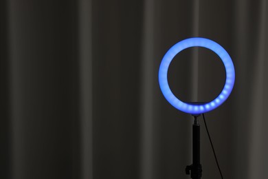 Photo of One glowing ring lamp near black curtain. Space for text