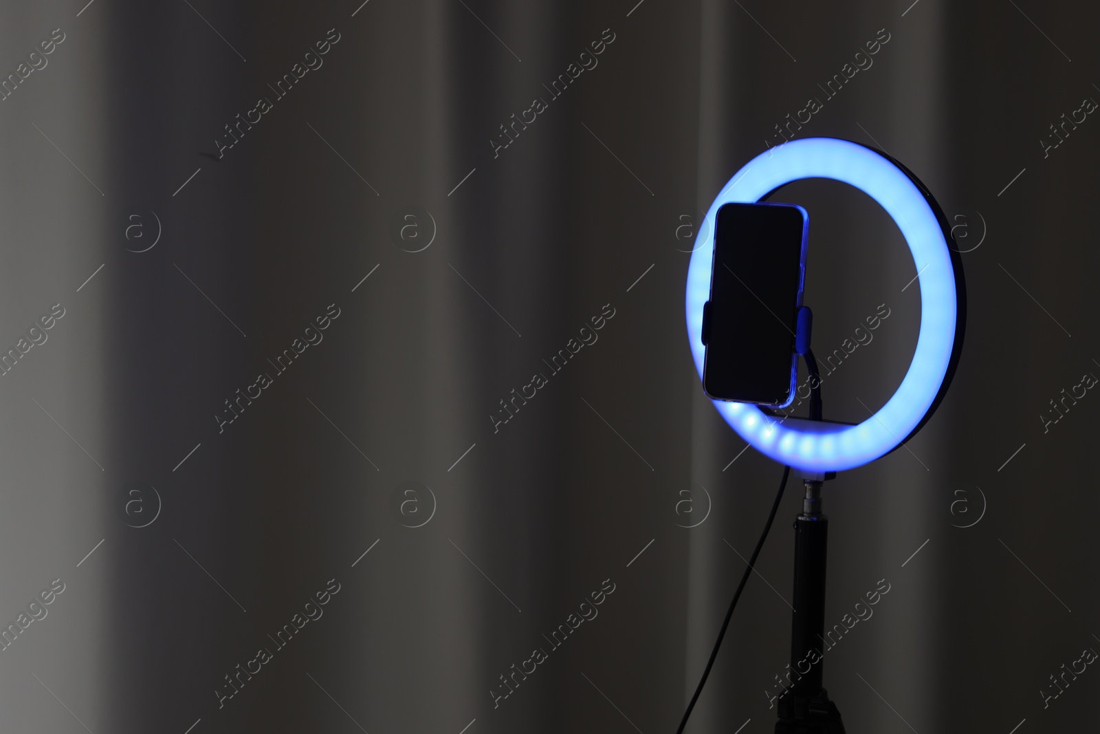 Photo of Glowing ring lamp with smartphone near black curtain. Space for text