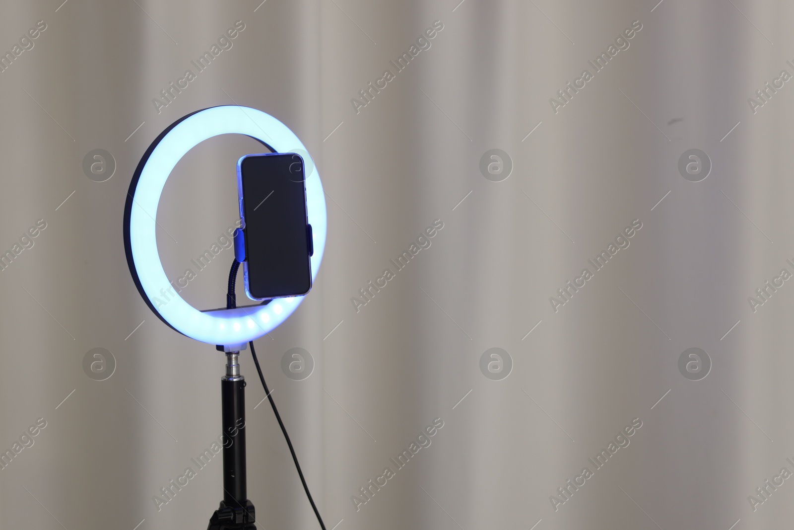 Photo of Glowing ring lamp with smartphone near light curtain. Space for text