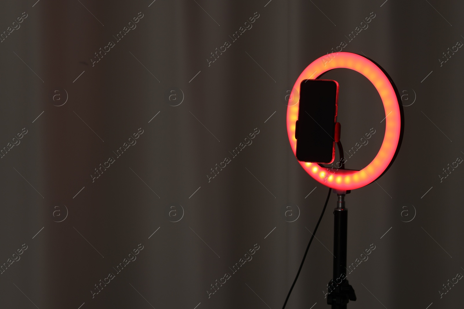 Photo of Glowing ring lamp with smartphone near grey curtain. Space for text