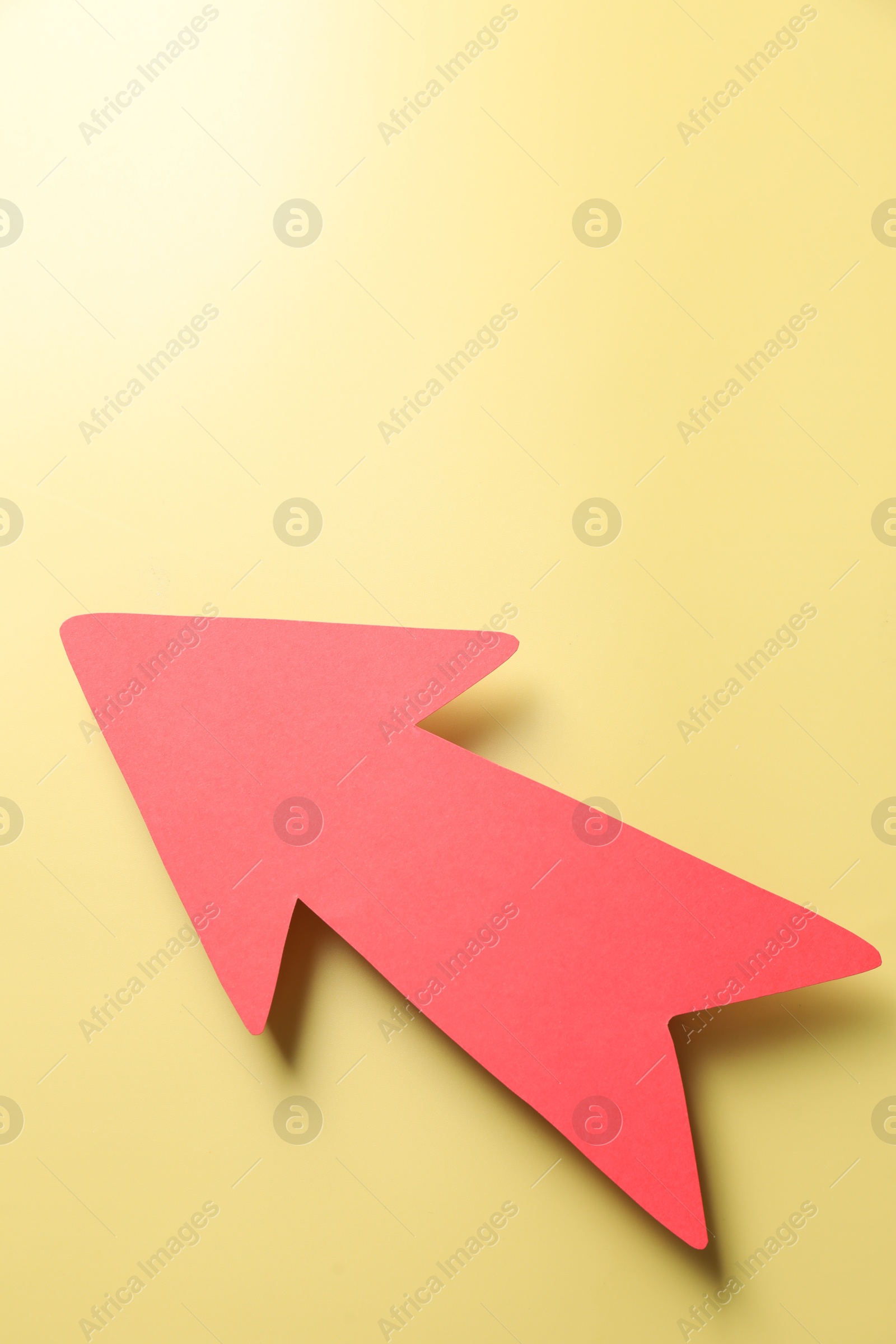 Photo of One red paper arrow on yellow background, top view