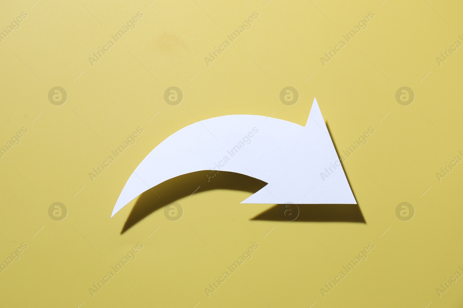 Photo of One white paper arrow on yellow background, top view