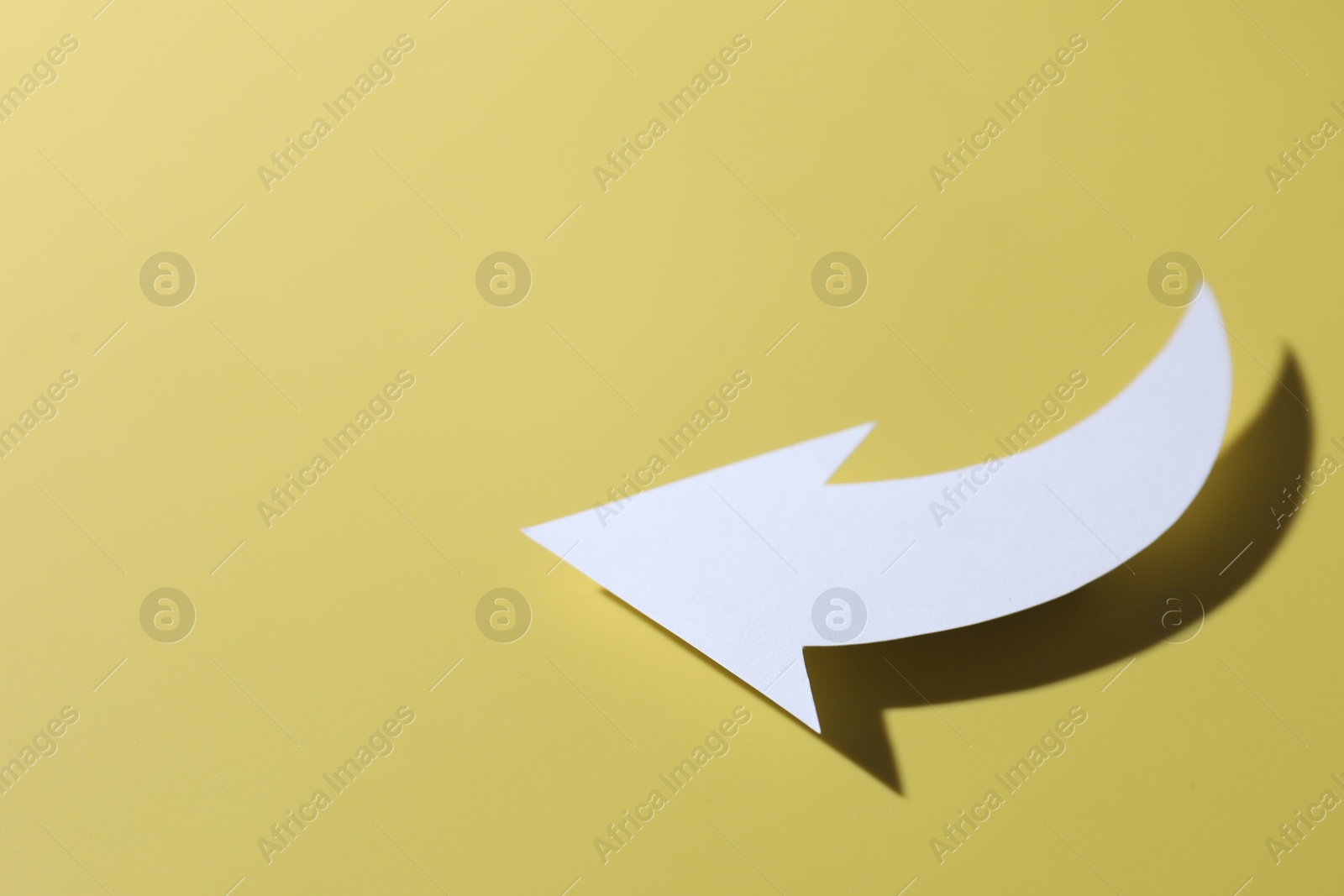 Photo of One white paper arrow on yellow background. Space for text