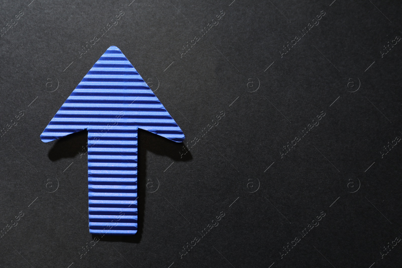 Photo of One blue paper arrow on black background, top view. Space for text