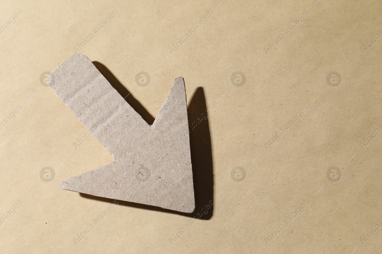 Photo of One paper arrow on kraft background, top view. Space for text