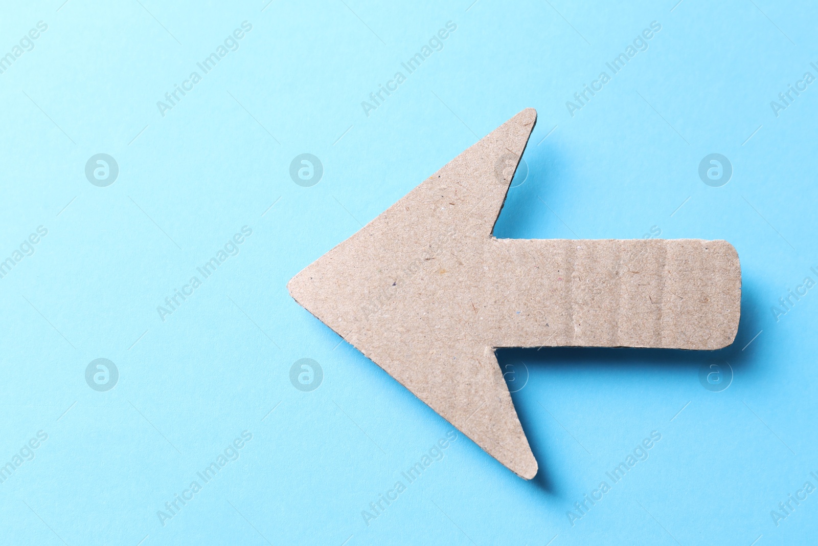 Photo of One kraft paper arrow on light blue background, top view. Space for text