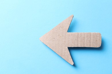 Photo of One kraft paper arrow on light blue background, top view. Space for text