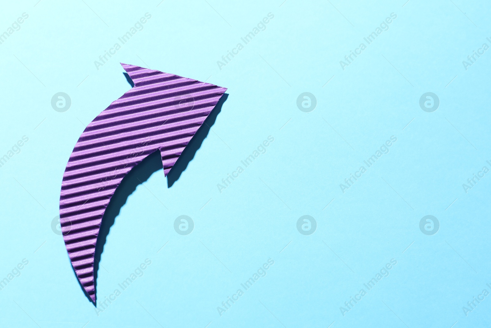 Photo of One purple paper arrow on light blue background, top view. Space for text