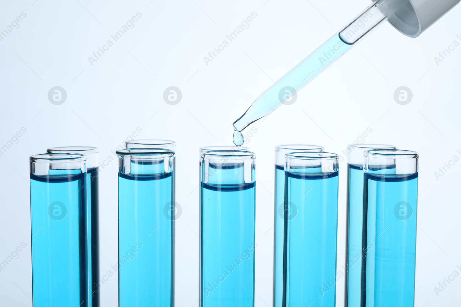 Photo of Dripping liquid into test tubes on white background