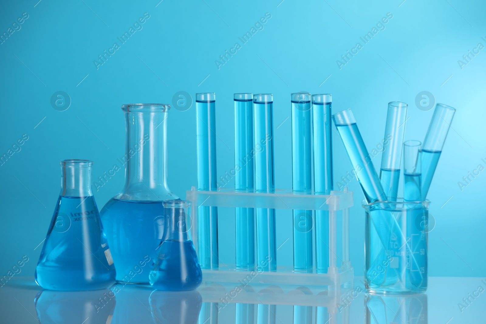 Photo of Laboratory glassware with liquid on mirror surface against blue background