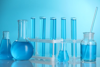 Photo of Laboratory glassware with liquid on mirror surface against blue background