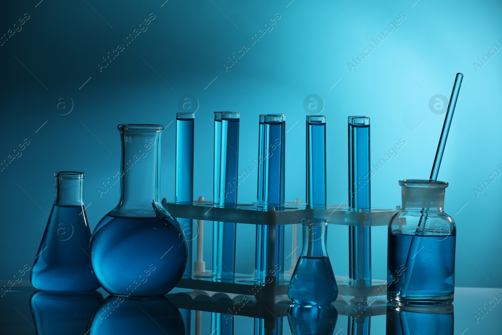 Photo of Laboratory glassware with liquid on mirror surface against blue background