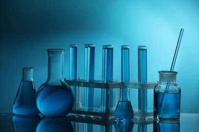 Photo of Laboratory glassware with liquid on mirror surface against blue background