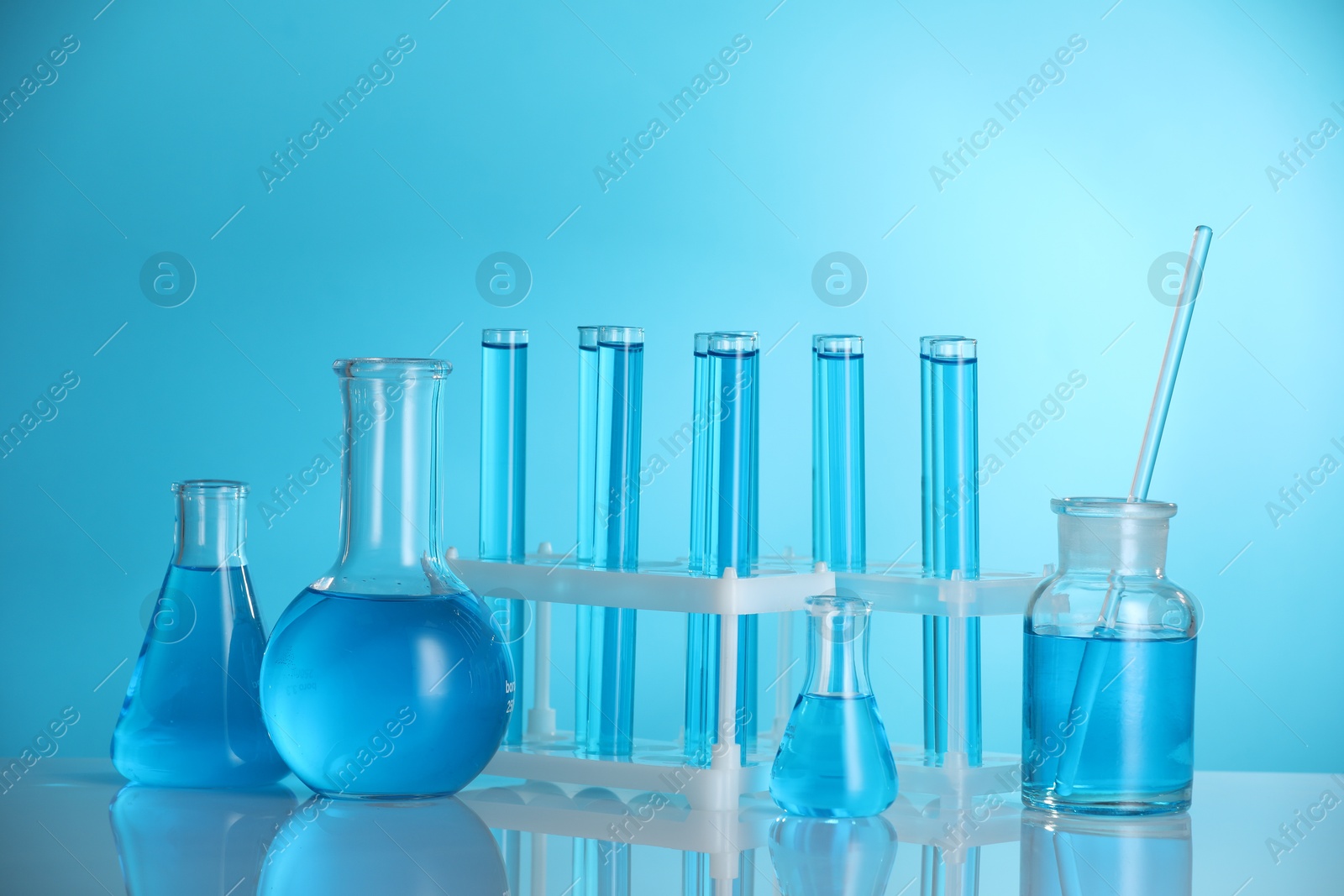 Photo of Laboratory glassware with liquid on mirror surface against blue background