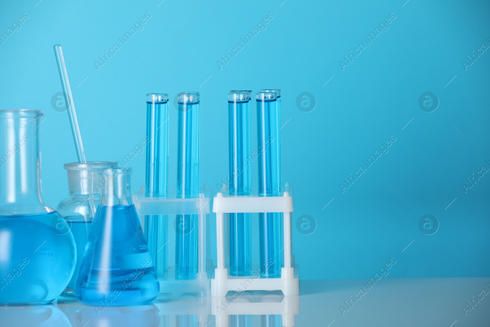 Photo of Laboratory glassware with liquid on mirror surface against blue background. Space for text