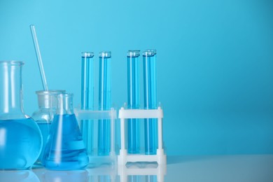 Photo of Laboratory glassware with liquid on mirror surface against blue background. Space for text