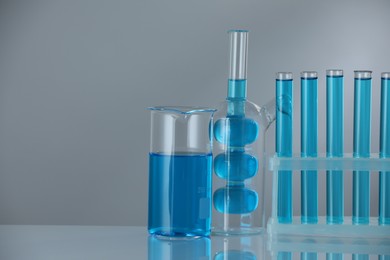 Photo of Laboratory glassware with blue liquid on mirror surface against grey background. Space for text