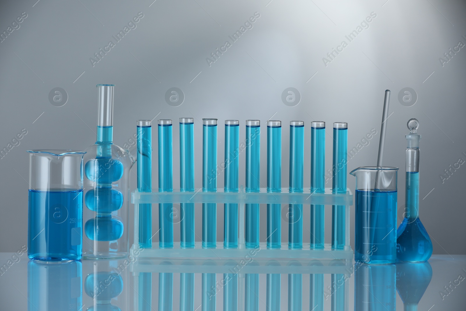 Photo of Laboratory glassware with blue liquid on mirror surface against grey background