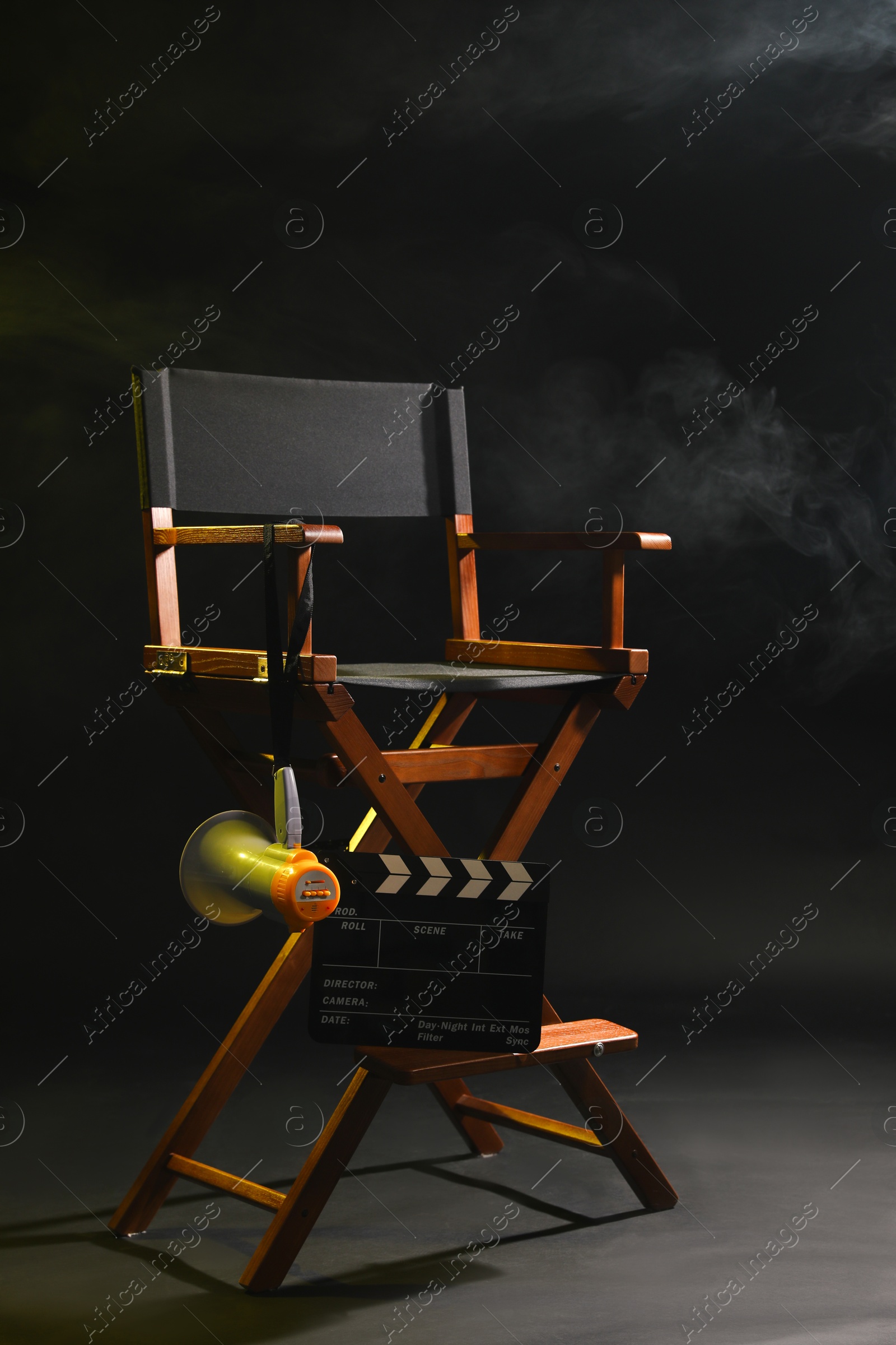 Photo of Director's chair with clapperboard and megaphone on dark background with smoke