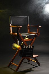 Photo of Director's chair with clapperboard and megaphone on dark background with smoke