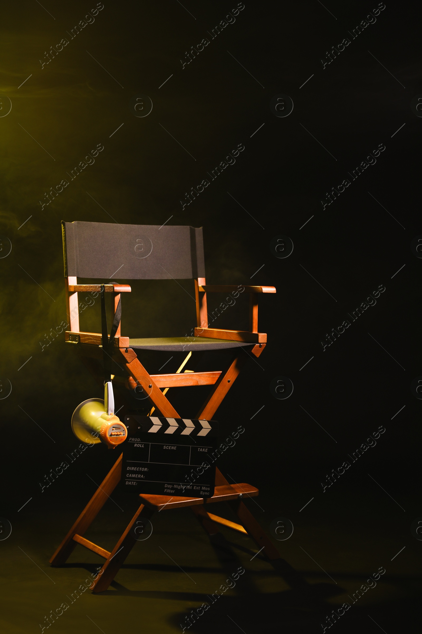 Photo of Director's chair with clapperboard and megaphone on dark background with smoke