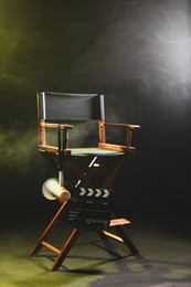 Photo of Director's chair with clapperboard and megaphone on dark background with smoke