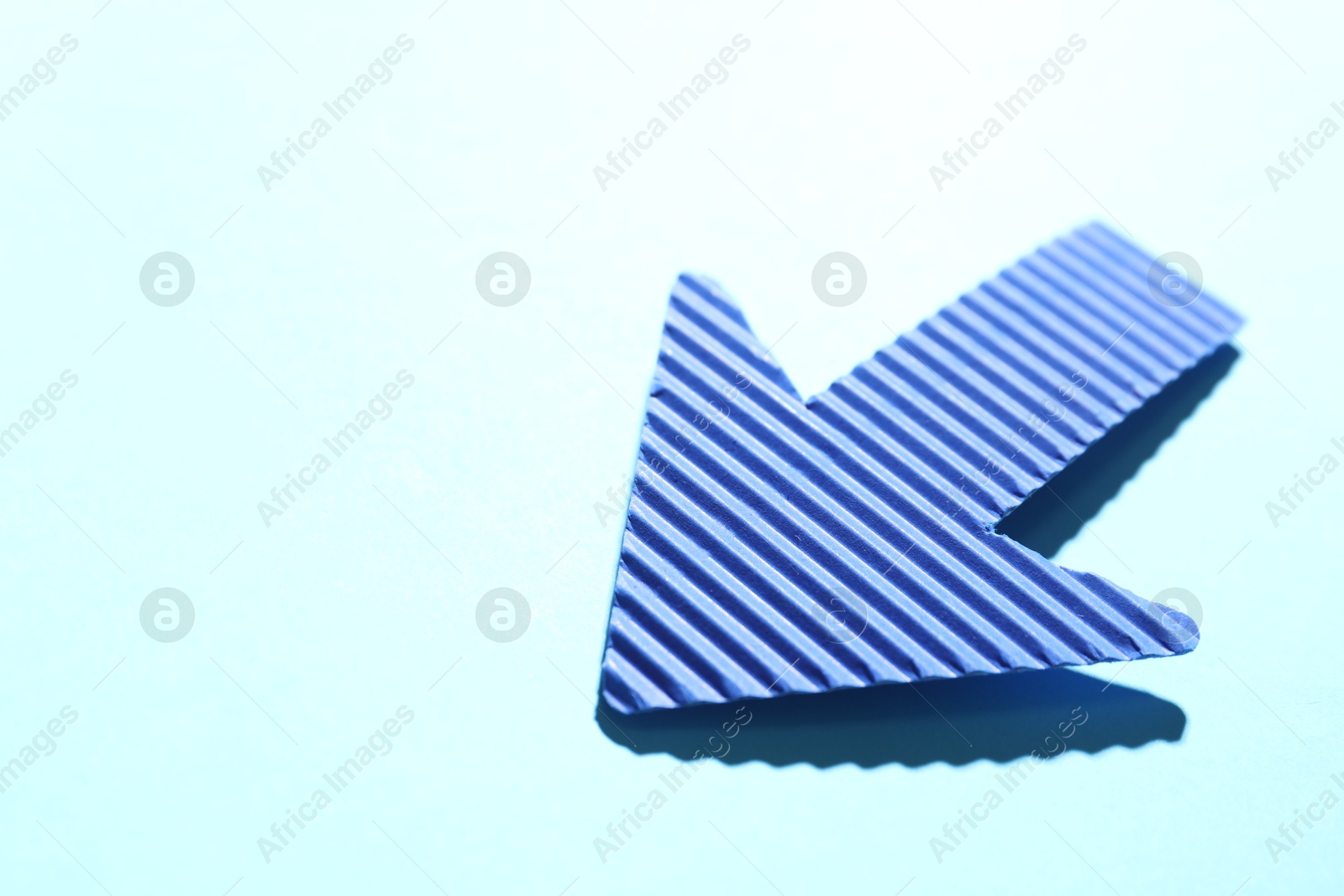 Photo of One paper arrow on light blue background, closeup. Space for text