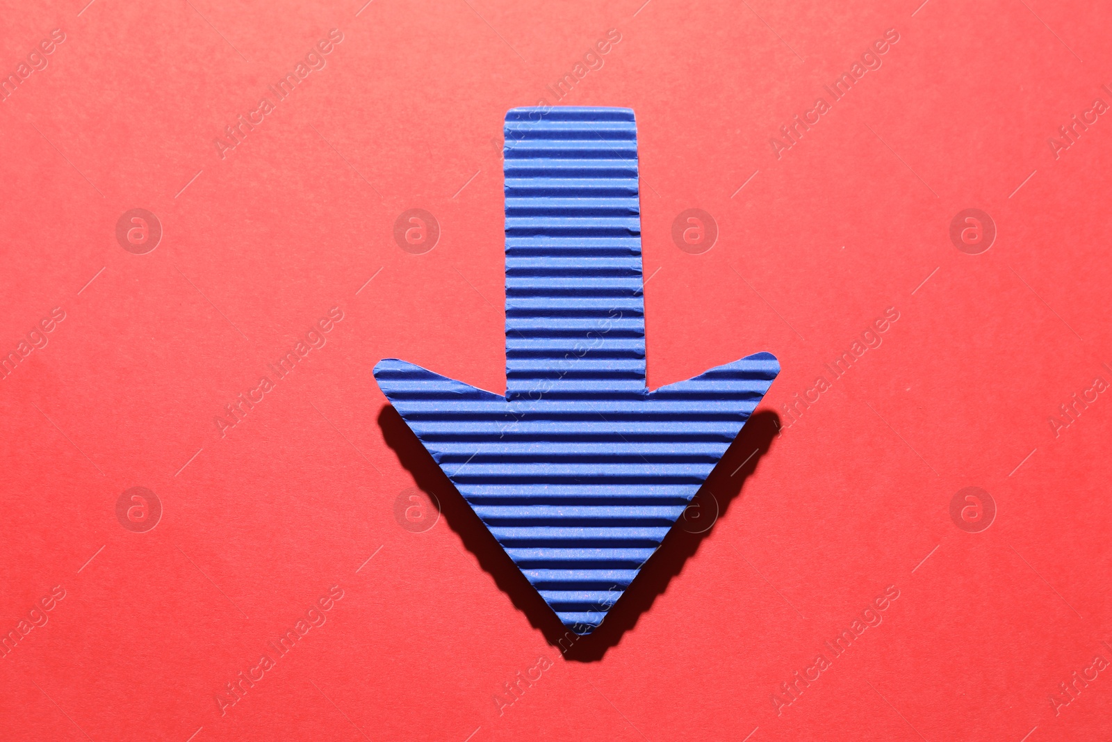 Photo of One blue paper arrow on red background, top view