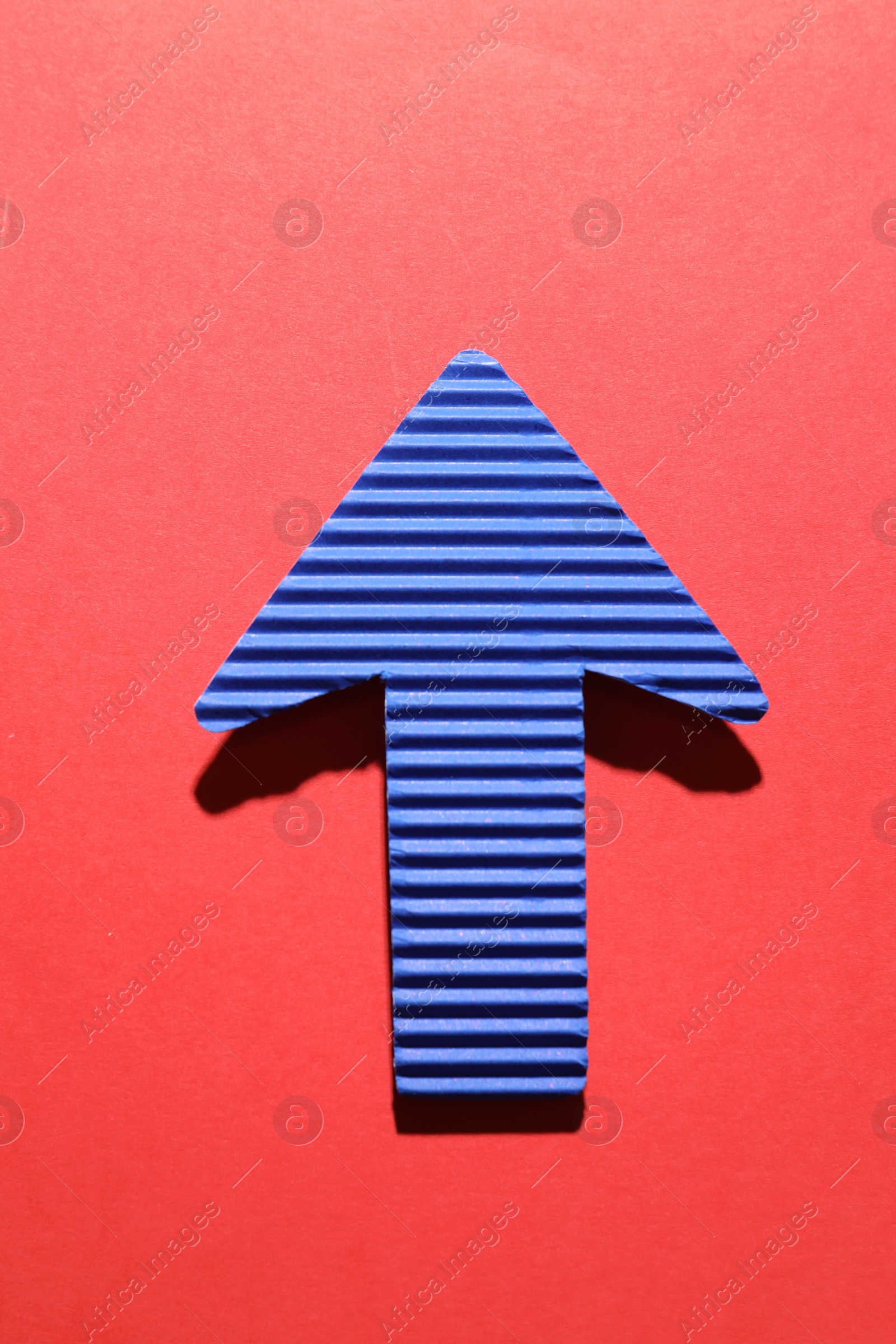 Photo of One blue paper arrow on red background, top view