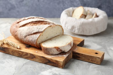 Photo of Wooden cutting board with fresh bread and spikes on grey table, closeup