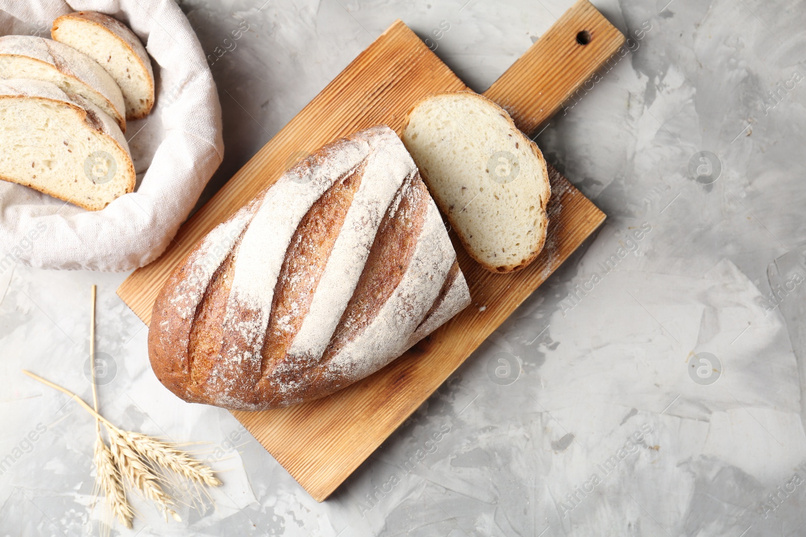 Photo of Wooden cutting board with fresh bread and spikes on grey table, flat lay. Space for text