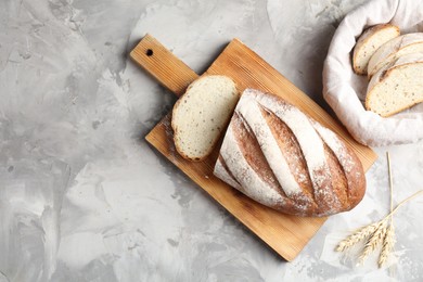 Photo of Wooden cutting board with fresh bread and spikes on grey table, flat lay. Space for text