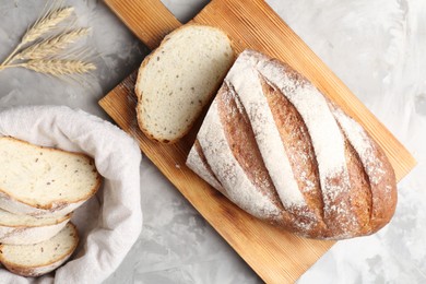 Photo of Wooden cutting board with fresh bread and spikes on grey table, flat lay