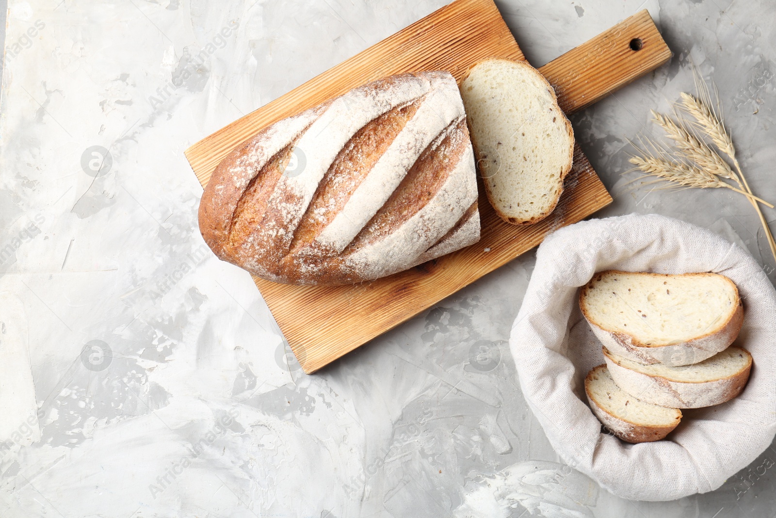 Photo of Wooden cutting board with fresh bread and spikes on grey table, flat lay. Space for text